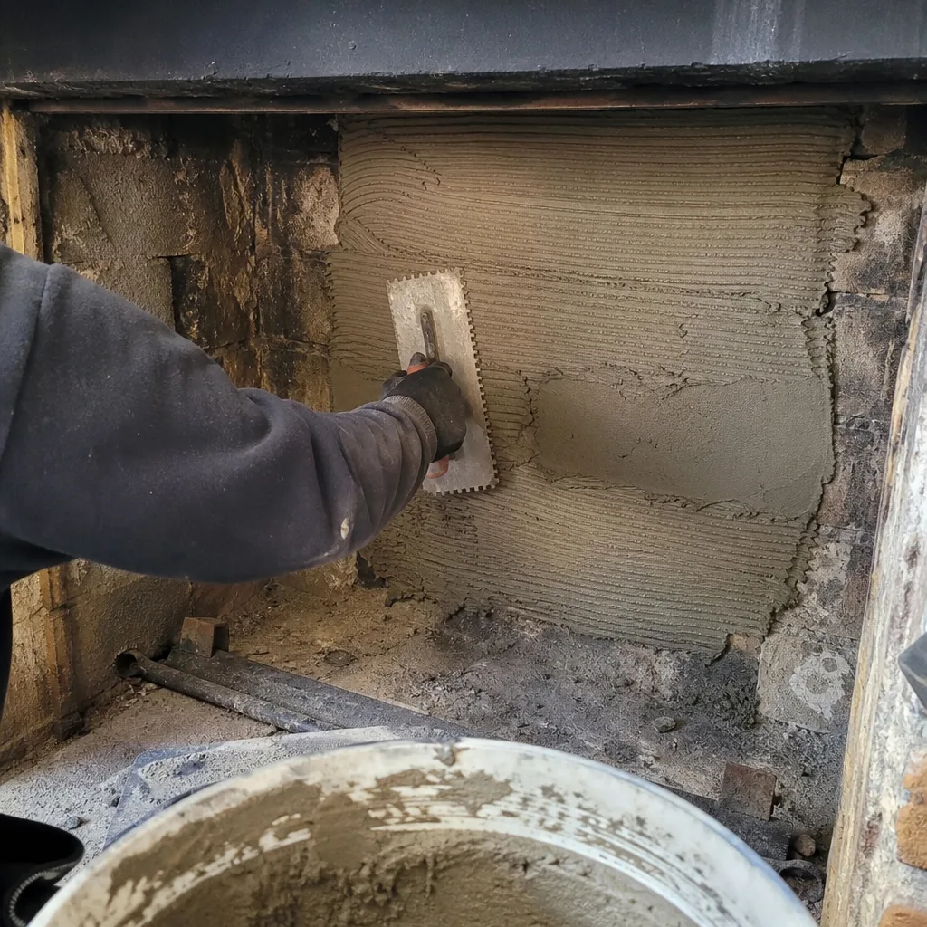Worker applying mortar to a fireplace wall with a notched trowel